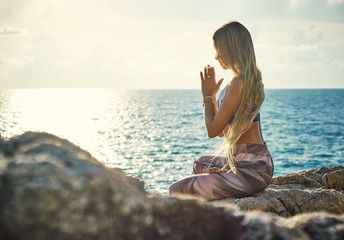 Young blonde woman doing yoga on the cliff by the sea at sunrise     
