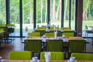 Empty restaurant part of hotel with table and armchair near windows and garden view.