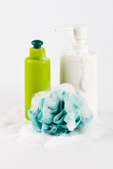 Bath cosmetic products, green sponge and foam on light background.