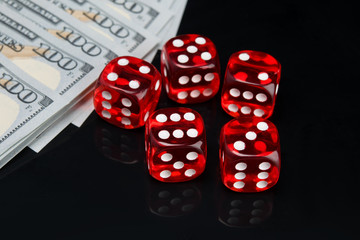 on a black background with a reflection, five red dice for the game and hundred dollar bills laid out in a row