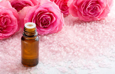 Fototapeta na wymiar Bottle with essential oil , spa salt crystals and pink roses.