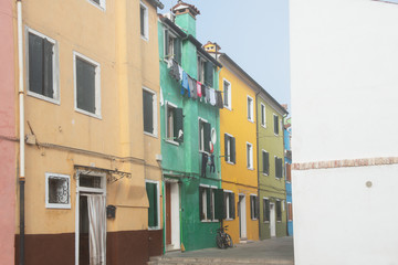 Fototapeta na wymiar Colorful houses on the Italian island Burano, province of Venice, Italy. Multicolored buildings in fog, Italian courtyard with dry laundry outdoor.