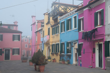 Colorful houses on the Italian island Burano, province of Venice, Italy. Multicolored buildings in fog, Italian courtyard with dry laundry outdoor.