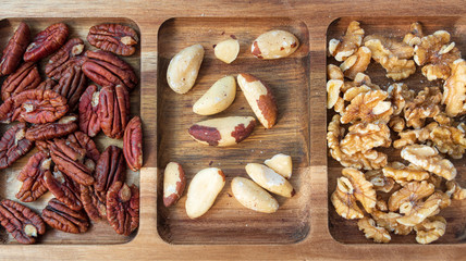 Selection of different types of nuts on wooden plate: pecan nuts, brazil nuts, walnuts. Healthy organic food rich in protein, fiber, minerals and vitamins.