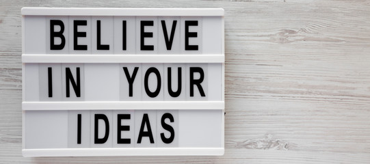 'Believe in your ideas' words on a modern board over white wooden background. Flat lay, from above, overhead. Copy space.