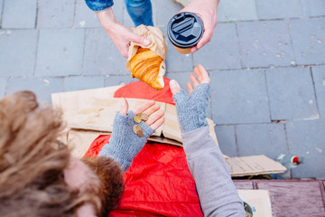 Croissant from stranger. Share food with hungry unhappy lonely man. Close up of unidentified man's hands giving homeless beggar some hot drink and food bread outdoors. Concept of helping poor people