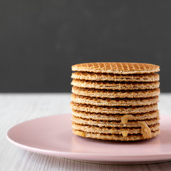 Stack of homemade Dutch stroopwafels with honey-caramel filling on a pink plate, side view. Closeup.
