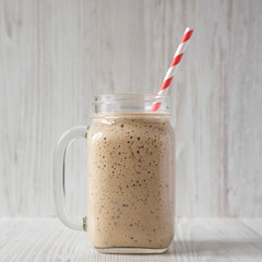 Homemade banana, kiwi, apple smoothie in a glass jar over white wooden surface, side view.
