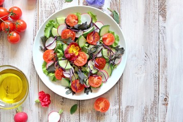Fresh vegetables salad: tomato, lettuce, cucumber and raw on light background. Top view with copy space.