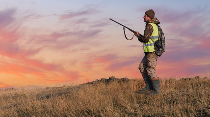 Silhouette of a hunter with a gun in the reeds against the sun, an ambush for ducks with dogs	