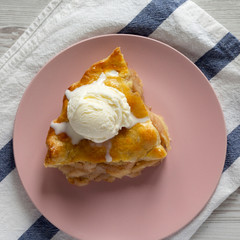 Slice of homemade apple pie with vanilla ice cream on a pink plate, overhead view. From above, top view, flat lay.