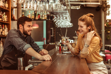 Red-haired woman talking to bartender while holding a cocktail