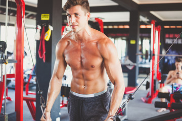 Fototapeta na wymiar portrait of young handsome guy with tanned fit naked torso doing a crossover exercise with blocks in the gym. tense face and body
