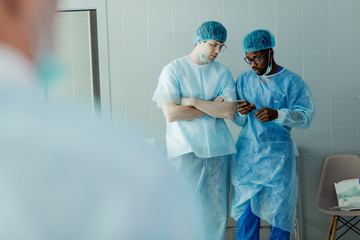 Fototapeta premium serious attractive doctors talking and using smart phone while working. close up photo. gadget concept. afro young man browsing the net , showing information to his colleague from mobile phone