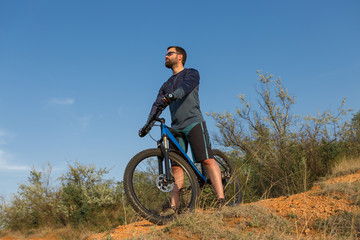 Fototapeta premium Cyclist in shorts and jersey on a modern carbon hardtail bike with an air suspension fork rides off-road on the orange-red hills at sunset evening in summer 