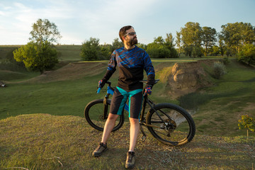 Obraz premium Cyclist in shorts and jersey on a modern carbon hardtail bike with an air suspension fork rides off-road on green hills near the forest 