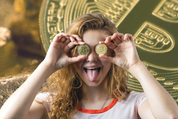Woman holding a physical bitcoin in her hand on gray background. Emotional portrait of a girl with cryptocurrency.