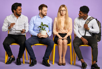 Fototapeta premium multinational team sitting together and looking at pretty girl in glasses. Young man with house plant looking jealous waiting for job interview