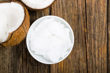 pile of rigid coconut oil on china dish and broken coconut shells, old wood table