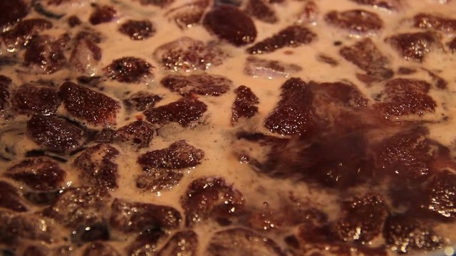 Preparation of strawberry jam. Cook jam. Homemade berry jam gradually boils in a large flat saucepan close up. A woman's hand with a ladle neatly stirs it. Traditional cuisine