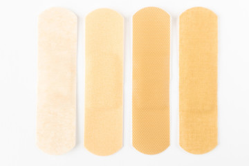Adhesive plasters of various skin tones from light beige to saturated. A set of adhesive plasters on a white background. Necessary items for summer activities, treatment of wounds, scratches.