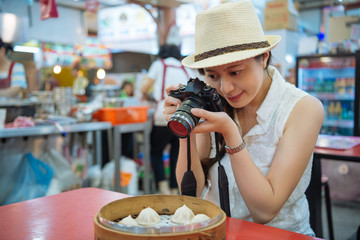 japanese girl traveler favorite taiwanese food Xiao Long Bao in bamboo steamer box. young asian woman photogrpaher taking picture from camera with pork dumpling sitting in local vendor eating smiling