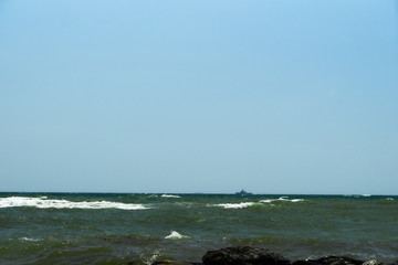 Image of the sea shore. In the background is a warship.