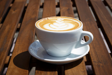 Hot cappuccino with froth and pattern on wooden background, side view