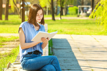 Beautiful young woman reading book in park