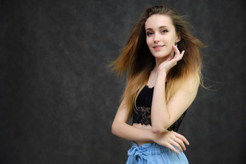 Photograph of a portrait of a beautiful girl woman with long dark flowing hair, happy life on a dark gray background. She is standing directly in front of the camera in various poses and smiling.