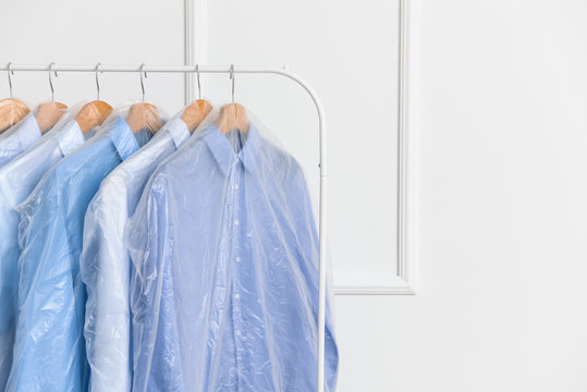 Rack with clothes after dry-cleaning near white wall