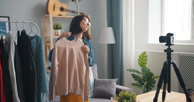 Pretty blogger female stylist is recording video about fashionable clothes talking using camera at home demonstrating new trends. People, vlogging and youth concept.