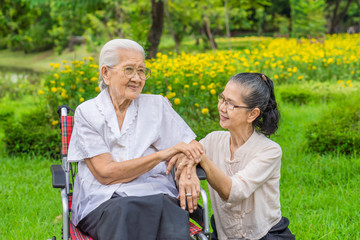 Cheerful senior daughter taking care of her mother in wheelcahir in garden. They are Asian peoples in Thailand.