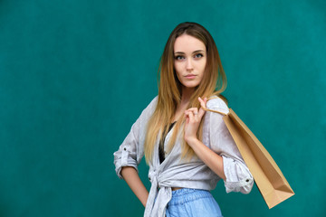 Photograph of a portrait of a beautiful girl woman with long dark flowing hair, loves shopping, on a green background with packages from the store. She is standing in different poses and smiling.