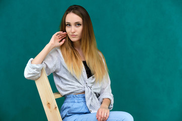 Picture a portrait of a beautiful girl woman with long dark flowing hair, fashionable, on a green background sitting on a wooden staircase. She sits in different poses and smiles.