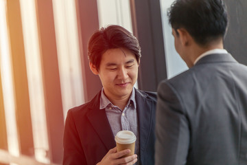 Young Asian leader businessman professional look talking together in the office with hot coffee cup in hand