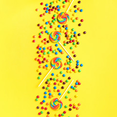 Multicolored lollipop, rainbow colorful candies on yellow background. Coated chocolate sweet pieces texture. Top view. Flat lay. Confetti for holidays, birthday party concept