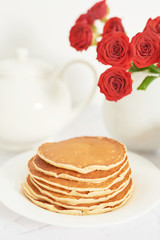 Obraz na płótnie Canvas Independence Day on July 4th, American pancakes on the table next to the crockery and red roses.