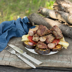 Grilled vegetables and juicy meat cooked on an open fire on wooden boards