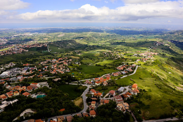 Fototapeta na wymiar panoramic view from top of Fortress Guaita on Mount Titano on city San Marino ,Italy with beautiful blue sky with clouds on sunny day. View towards the sea and over the San Marino villages and Rimini,