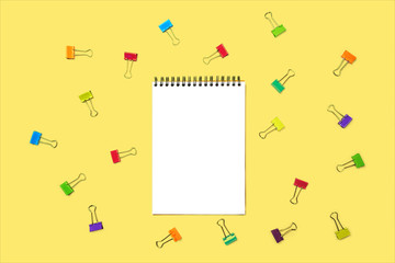 Back to school background with notepad, colorful paper clips on pastel yellow backdrop. Flat lay, top view, copy space.