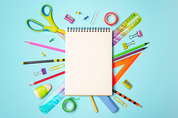 Back to school background with notepad, colorful pencils, square ruler, scissors, clips on pastel blue backdrop. Flat lay, top view, copy space.