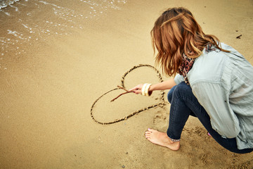 Girl drawing a heart in the sand of ocean / sea beach.