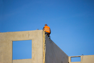 professional construction worker sits on the edge of the wall of a house under building...