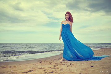 Fototapeta na wymiar Woman in a blue dress on the beach. Summer woman in a blue dress on the beach
