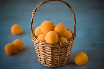 Ripe apricots to a brown basket on a gray background.