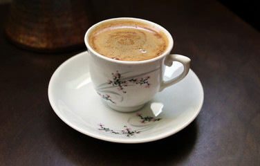 Cup of coffee on a dark background, with cooking pot