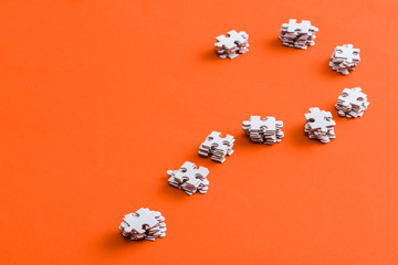 question mark shape with white jigsaw puzzle pieces on orange