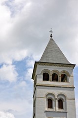 Bottom view of building turret with a cross on top on cloudy sky background.