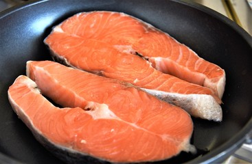 two pieces of raw salmon fish on a black skillet